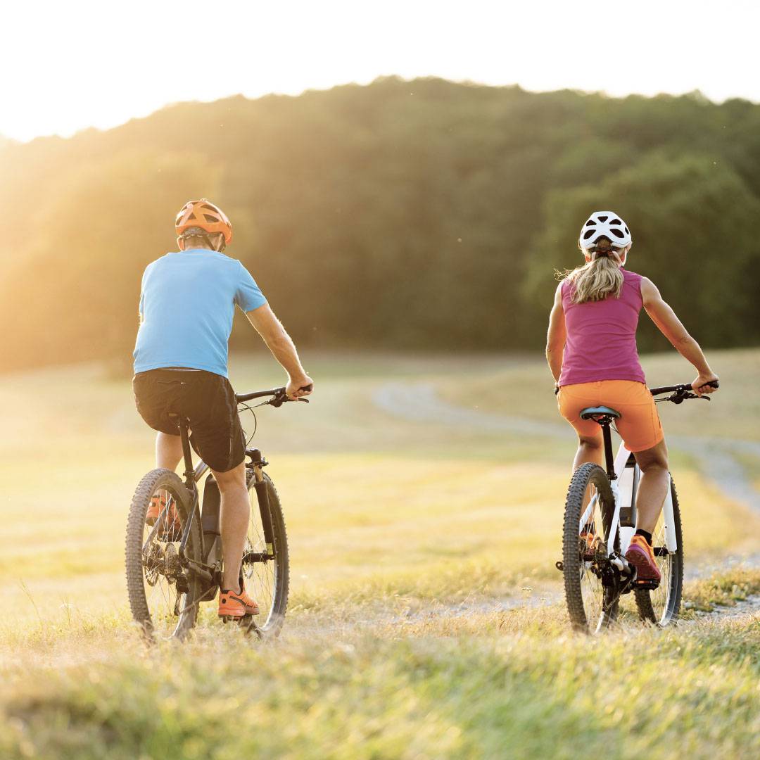 two people riding their bicycles in a field 